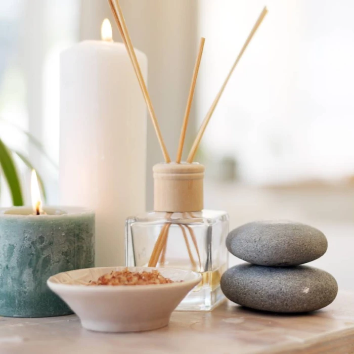A tranquil spa setting with a reed diffuser, stacked smooth stones, a bowl of bath salts, and lit candles, creating a serene atmosphere.