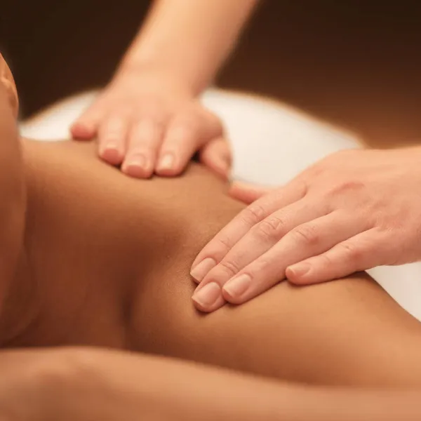 A close-up image of a person receiving a back massage, focusing on the masseuse's hands applying pressure to the recipient's skin.