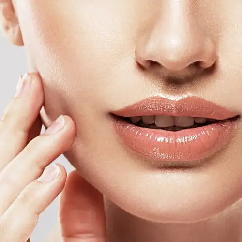 Close-up of a woman's lower face, highlighting her lips and chin, with a focus on her natural makeup look and a hand gently touching her cheek.