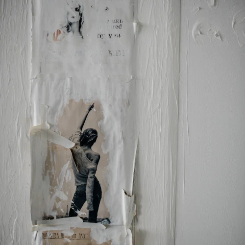 Close up of textured mixed-media artwork hung on a white wall. Some of the paper in the artwork is peeling, and the main subject is of a woman with her hand in the air.